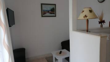 Un salon avec un téléviseur fixé au mur, une petite table blanche et une lampe dotée d’un pied décoratif.