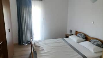 Un dormitorio con una cama, una mesita de noche con lámpara, una ventana con cortinas y una puerta de madera.