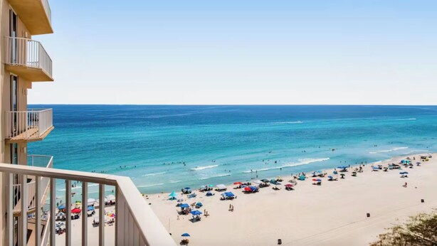 Una playa con aguas azules cristalinas, una orilla de arena y un edificio con balcones que dan a la playa.