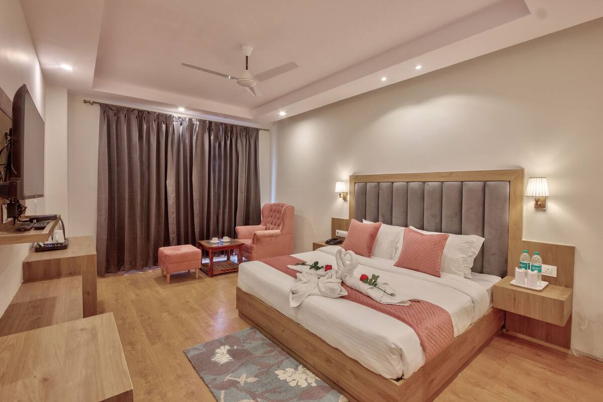 A modern hotel room with a large bed, a desk, a chair, a TV, and a ceiling fan.