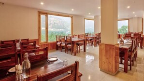 Un comedor amplio con varias mesas y sillas de madera, y ventanas grandes que ofrecen vistas a las montañas.