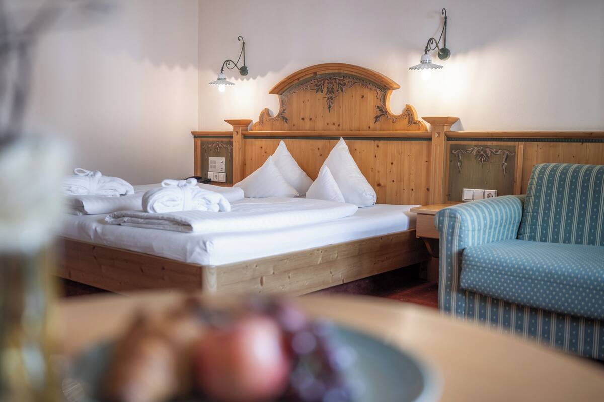 Ein Hotelzimmer mit einem Holzbett, zwei Nachttischlampen, einem blau gestreiften Sessel und einer Obstschale auf dem Tisch.