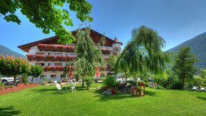 Ein Hotel mit rotem Dach, Balkonen mit Blumen, einem gepflegten Rasen und einem Berg im Hintergrund.