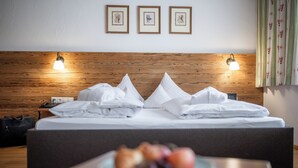 Ein ordentlich bezogenes Bett mit Kissen, ein Nachttisch mit Obstplatte und gerahmte Bilder an der Wand.