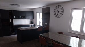 A modern kitchen with dark cabinets, a central island, and a large wall clock. - Villa Marija (Podstrana)