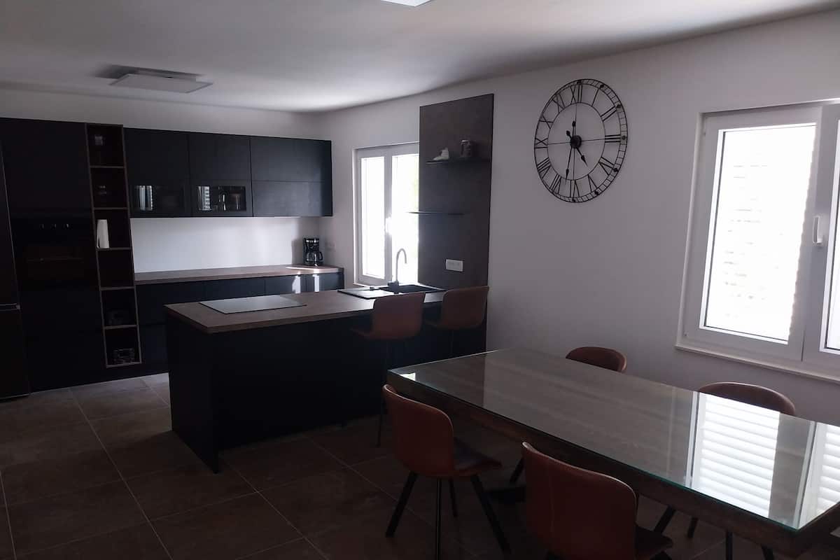 A modern kitchen with dark cabinets, a central island, and a large wall clock.