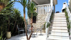 A stone staircase leading to a white balcony with metal chairs and a potted plant. - Villa Marija (Podstrana)