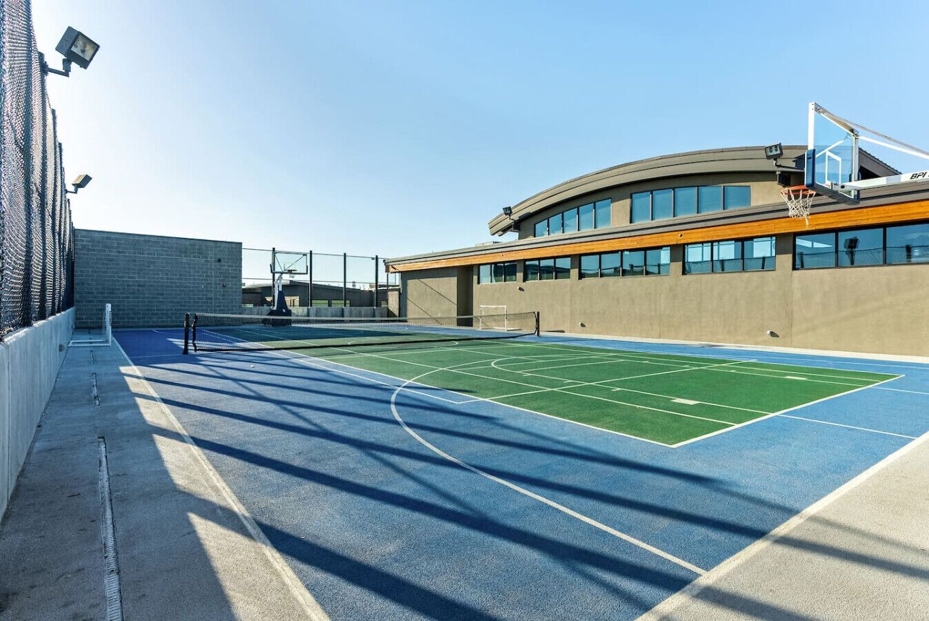 Una cancha de baloncesto al aire libre junto a un edificio de fachada curva y grandes ventanales.