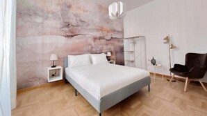 Un dormitorio moderno con una cama grande, una mesita de noche con lámpara, una silla y una pared con un mural texturizado.