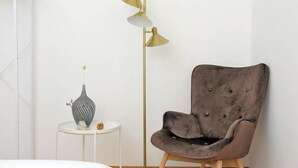 Una habitación con un sillón tapizado en gris, una lámpara de pie alta y una mesita blanca con un florero.
