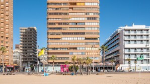 Een hotel aan het strand met meerdere verdiepingen, palmbomen en een helderblauwe lucht.