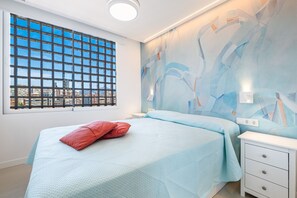A bedroom with a large window, a bed with a red pillow, a nightstand, and a wall with abstract art. - Principado Arena Levante Beach (Benidorm)