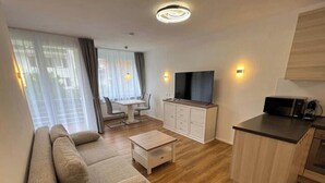 A modern living room with a sofa, a small table, a TV, and a kitchen area with a microwave. - Bergromantik Oberstdorf - Tiefenbach (Oberstdorf)