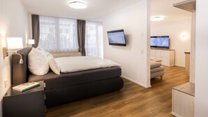 A modern bedroom with a bed, bedside tables, a TV, and a small seating area. - Bergromantik Oberstdorf - Tiefenbach (Oberstdorf)