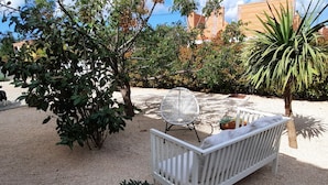 A white outdoor seating area with a woven chair and a bench, surrounded by various plants and trees. - Apartment Stella Casa Bruno (Vrsi)
