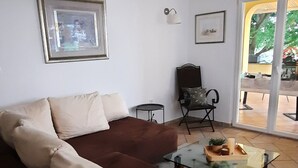 A living room with a brown sofa, a glass coffee table, a framed picture on the wall, a chair, and a view through a glass door. - Apartment Stella Casa Bruno (Vrsi)