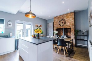 Een moderne keuken met een centraal eiland, een metselwerk openhaard en een eetgedeelte met een tafel en stoelen.