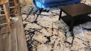 Een moderne woonkamer met een blauwe bank, een salontafel en een kamerbreed tapijt met dessin.