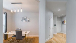 Un intérieur moderne avec un coin repas comprenant une table blanche, des chaises noires et un ordinateur portable. On y trouve également des lampes fixées au mur et une composition décorative d’assiettes.