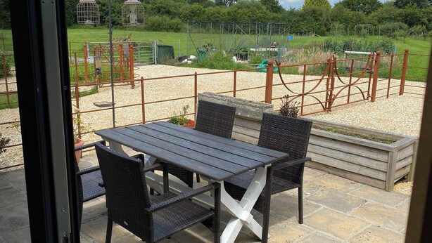 Eine Terrasse im Freien mit Tisch und Stühlen, einem Kiesbereich und einem umzäunten Garten.