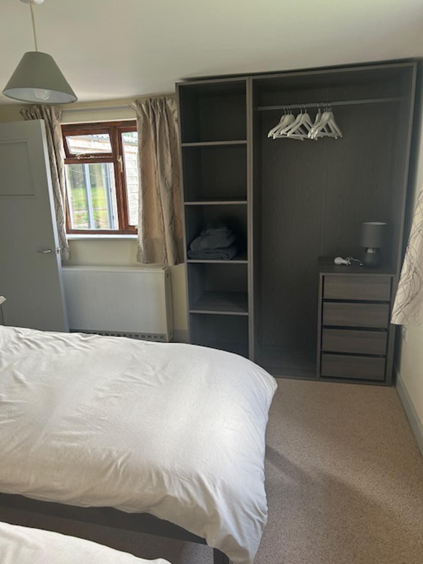 Une chambre à coucher comprenant un lit, une armoire, un radiateur, une fenêtre avec des rideaux et un luminaire suspendu.