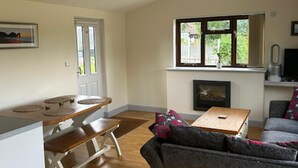 Ein Wohnzimmer mit einer hölzernen Bank, einem grauen Sofa, einem Kamin und einem Fenster mit Blick auf Grünflächen.