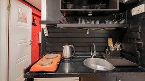 Una cocina compacta con encimera negra, una tetera, un lavabo y un escurreplatos.
