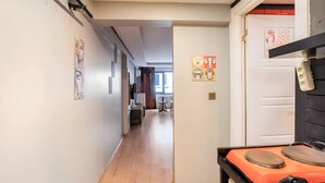 Un pasillo con suelo de madera, una zona de cocina con estufa naranja y obras de arte en las paredes.