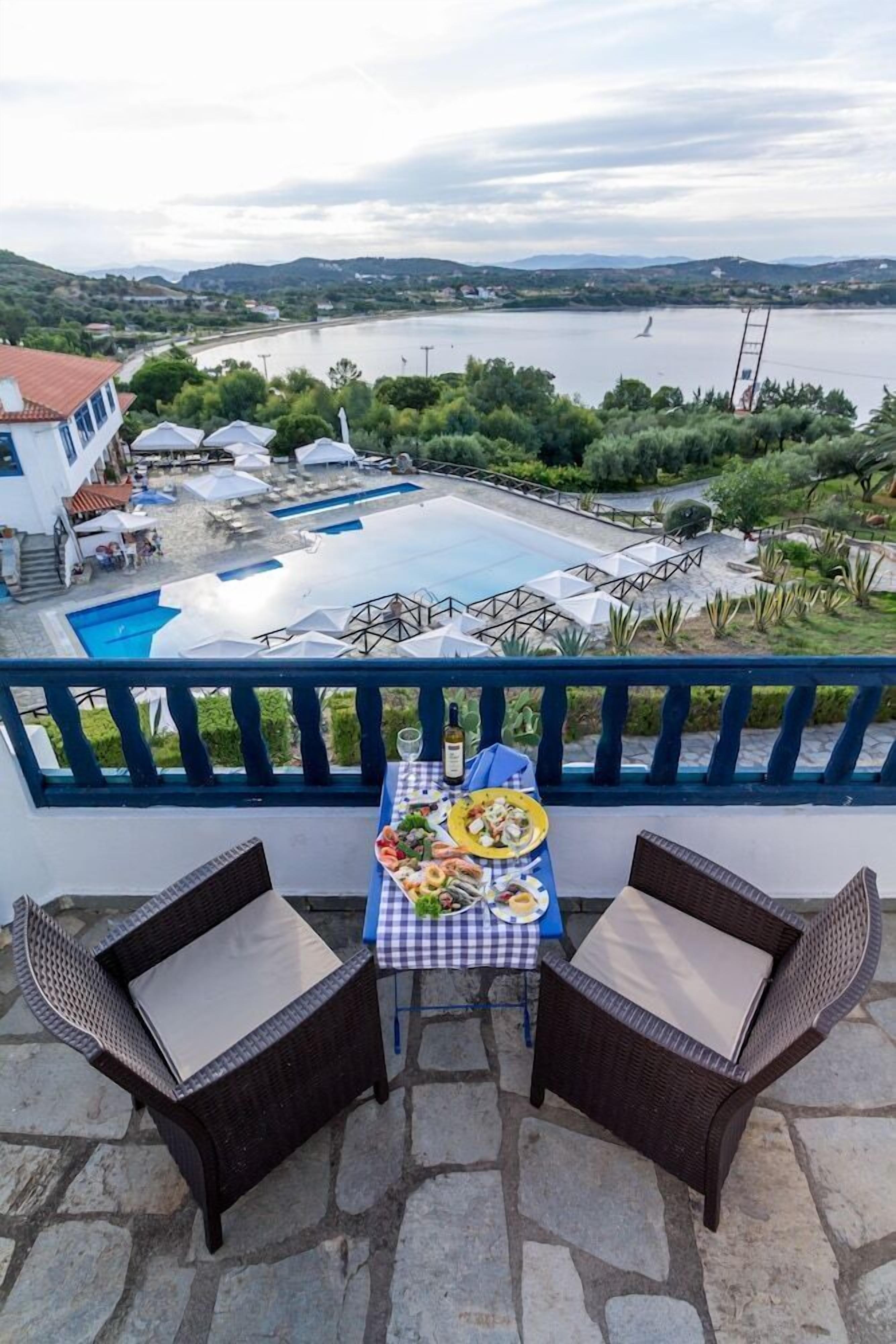 Una terraza con mobiliario de mimbre y una mesa preparada para comer, con vistas a una piscina y un lago.