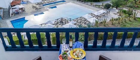 Una terraza con mobiliario de mimbre y una mesa preparada para comer, con vistas a una piscina y un lago.