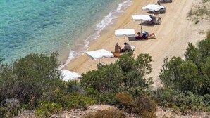 Een strand met helder turquoise water, witte parasols en enkele mensen die ontspannen.