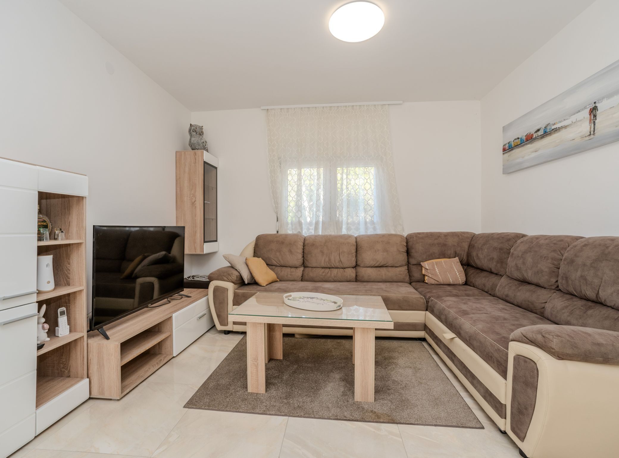 Un salon moderne avec un canapé d’angle, un téléviseur à écran plat, un meuble en bois et un tableau accroché au mur.