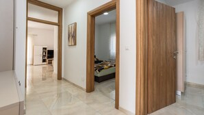 Un interior moderno con un pasillo que conduce a un dormitorio, una cama visible y una puerta.