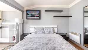 Ein Schlafzimmer mit Bett, Nachttisch, Radiator, Wandregal, gerahmtem Bild und weißem Kleiderschrank.