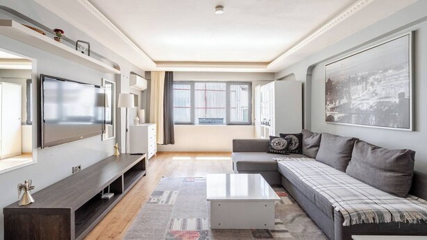 Ein modernes Wohnzimmer mit Flachbildfernseher, einer Couch, einem Couchtisch und einem großen Fenster mit Vorhängen.