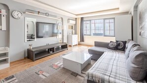 Ein modernes Wohnzimmer mit Flachbildfernseher, grauem Sofa, weißem Couchtisch und einem gemusterten Teppich.