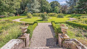 A garden pathway leading through a park with neatly trimmed hedges and a variety of plants.