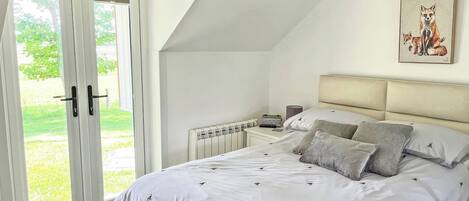 A bedroom with a large bed, a radiator, a bedside table, and a door leading to a balcony.