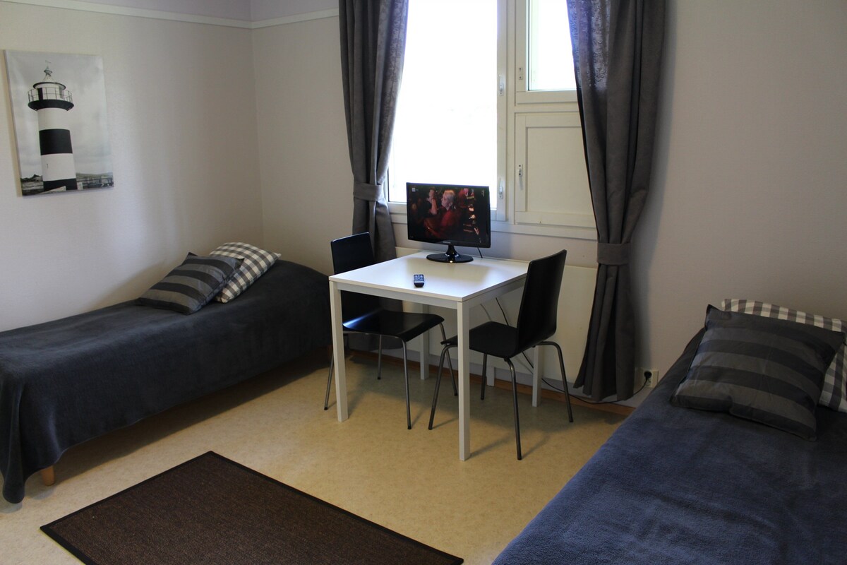 A room with two single beds, a small table with a computer, and a window with curtains.