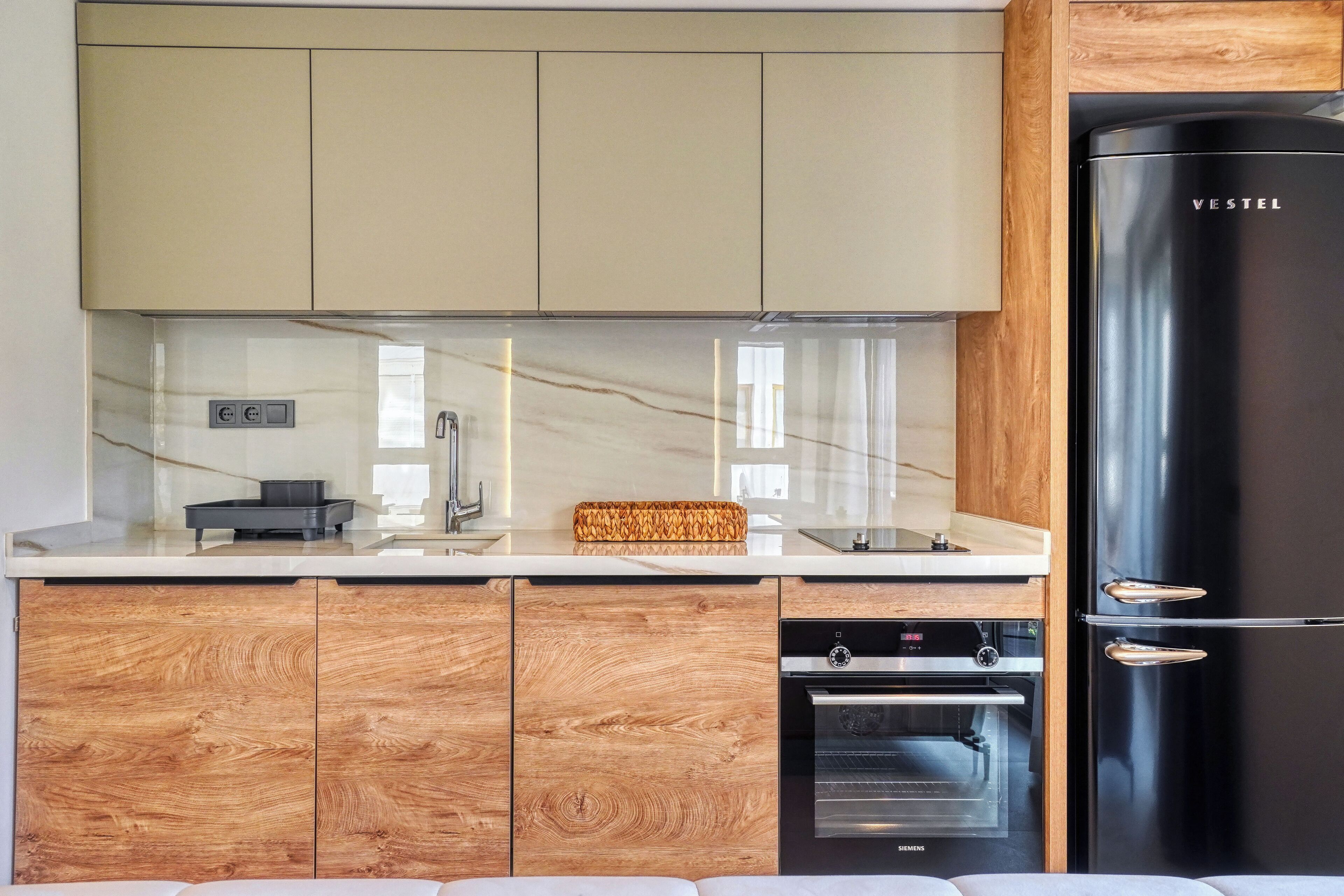 A modern kitchen with wooden cabinets, a black refrigerator, and a built-in oven.