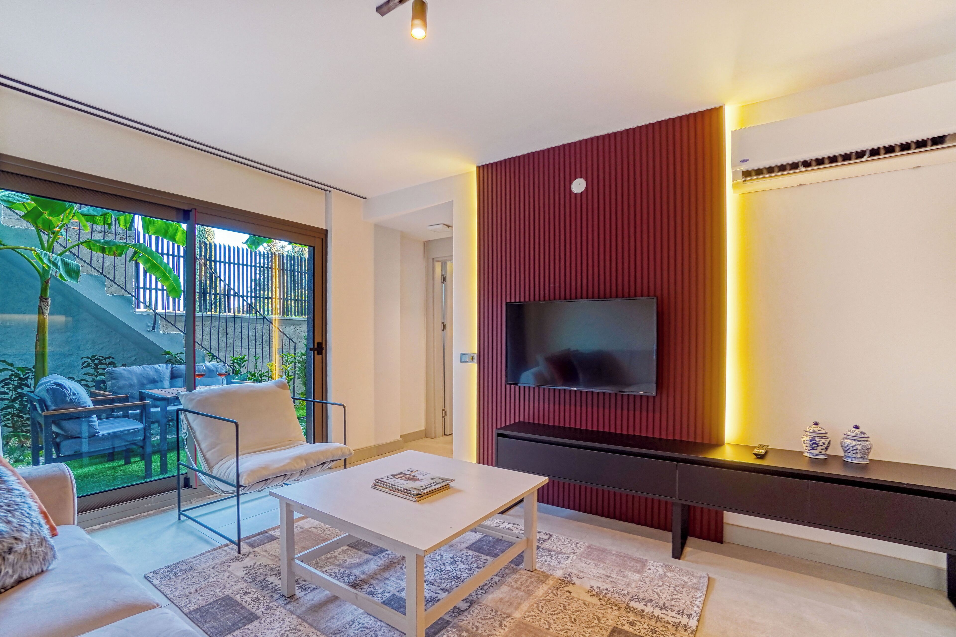 A modern living room with a TV mounted on a red wall, a white coffee table, and a sofa.