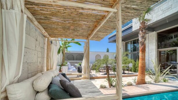 A poolside area with a wooden deck, a cushioned seating area, and a view of the pool and surrounding buildings. - Ayayorgi Homes & Suites (Cesme)