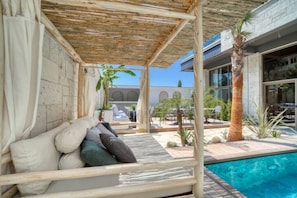 A poolside area with a wooden deck, a cushioned seating area, and a view of the pool and surrounding buildings. - Ayayorgi Homes & Suites (Cesme)