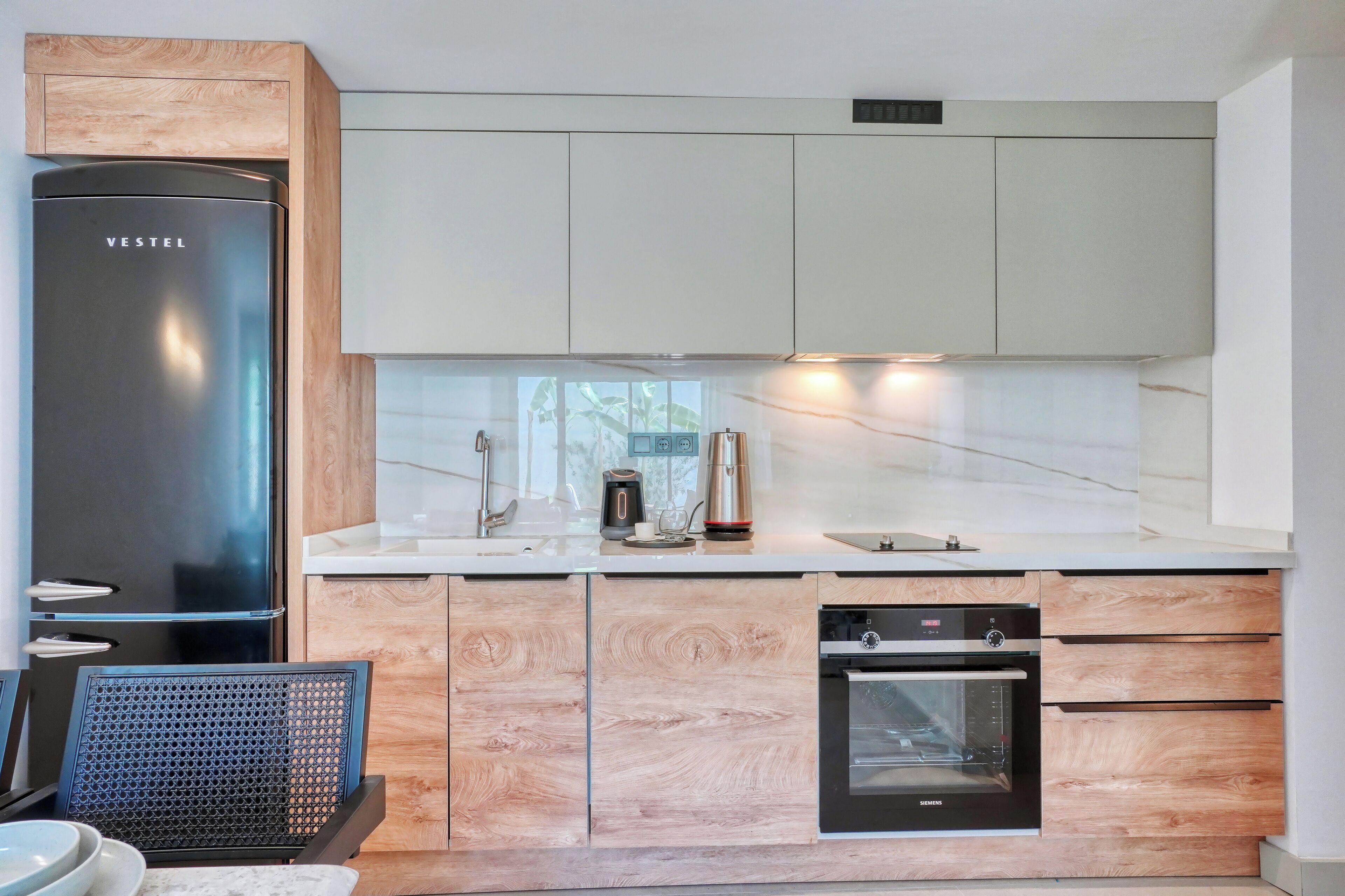 Una cocina moderna con un refrigerador de acero inoxidable, gabinetes de madera, un horno empotrado y una cafetera.