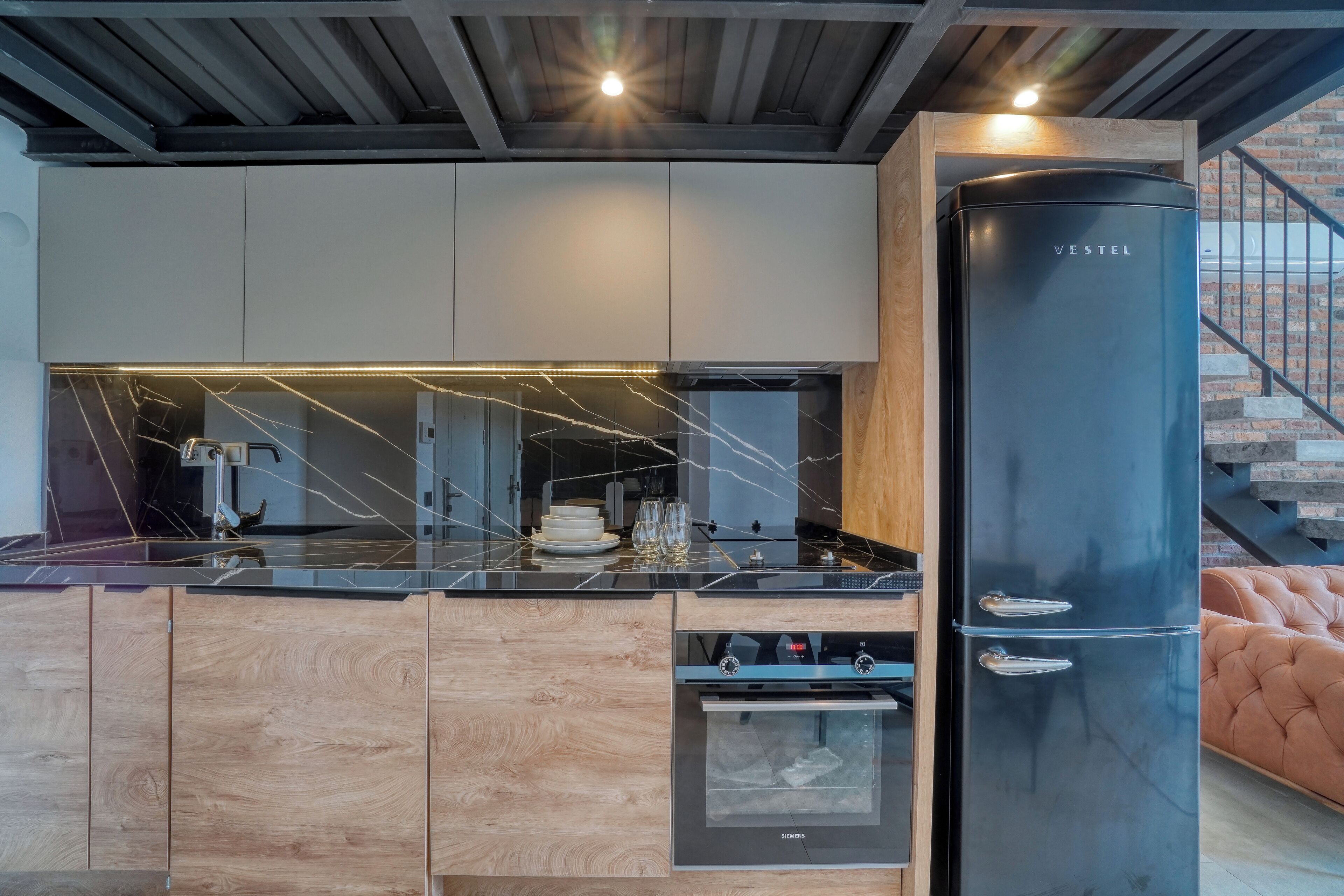 A modern kitchen with a black refrigerator, wooden cabinets, and a marble countertop.