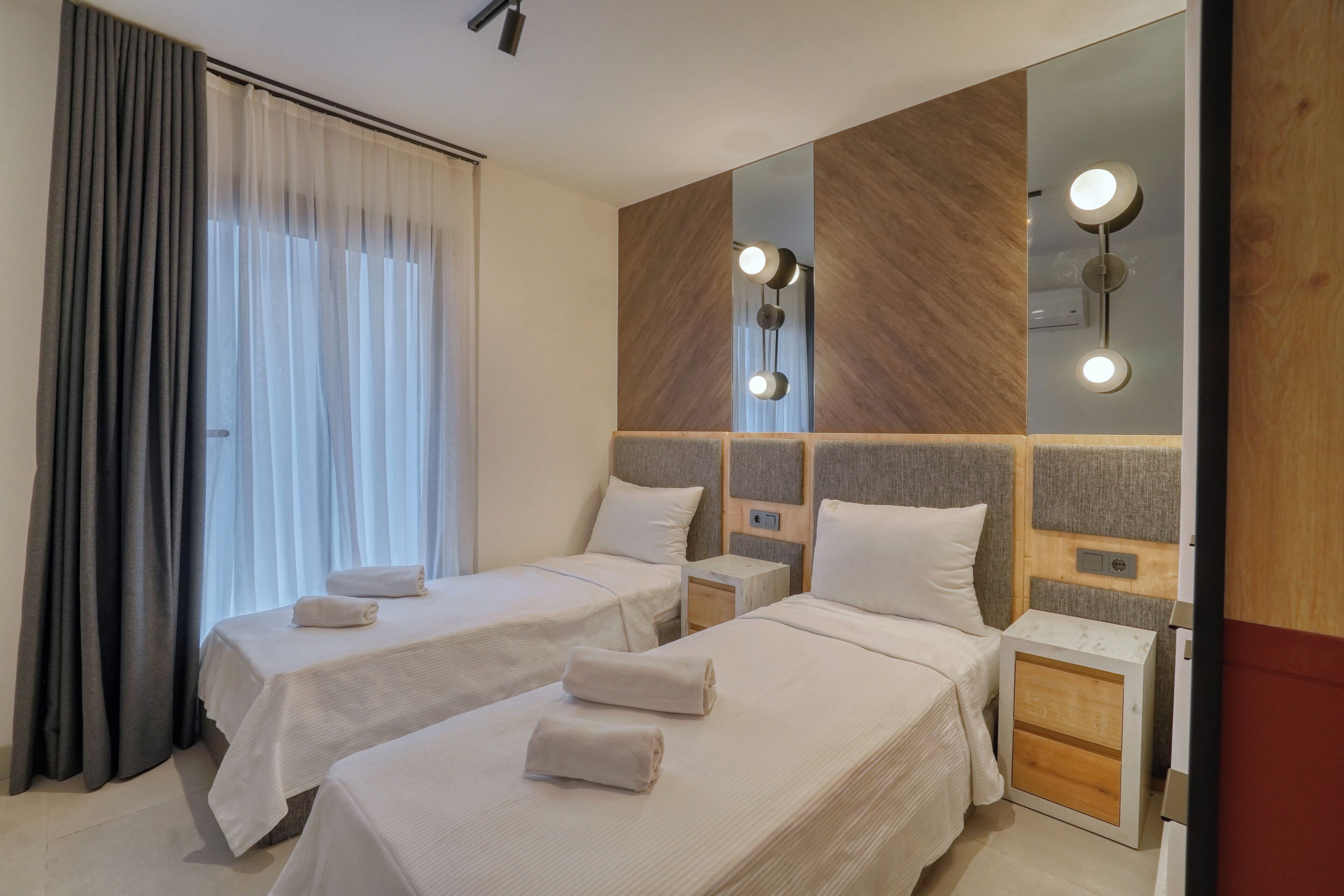 Habitación de hotel con dos camas, una mesita de noche, un espejo y una ventana con cortinas.