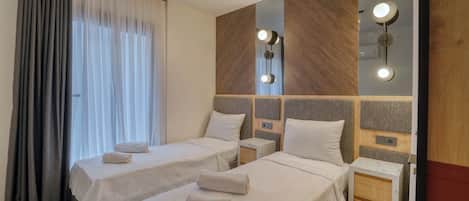 Habitación de hotel con dos camas, una mesita de noche, un espejo y una ventana con cortinas.