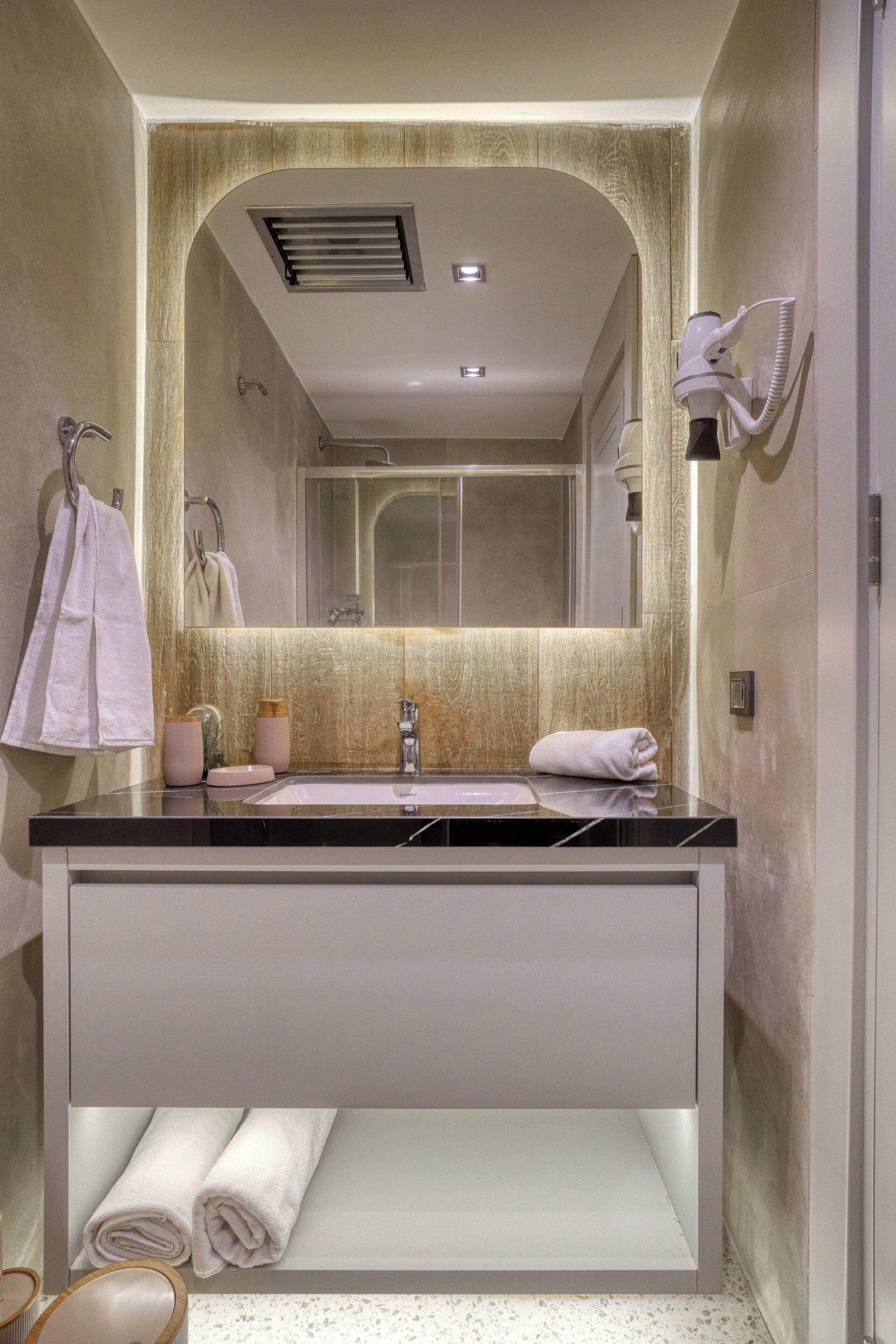 A modern bathroom with a large mirror, a sink, and a towel rack.