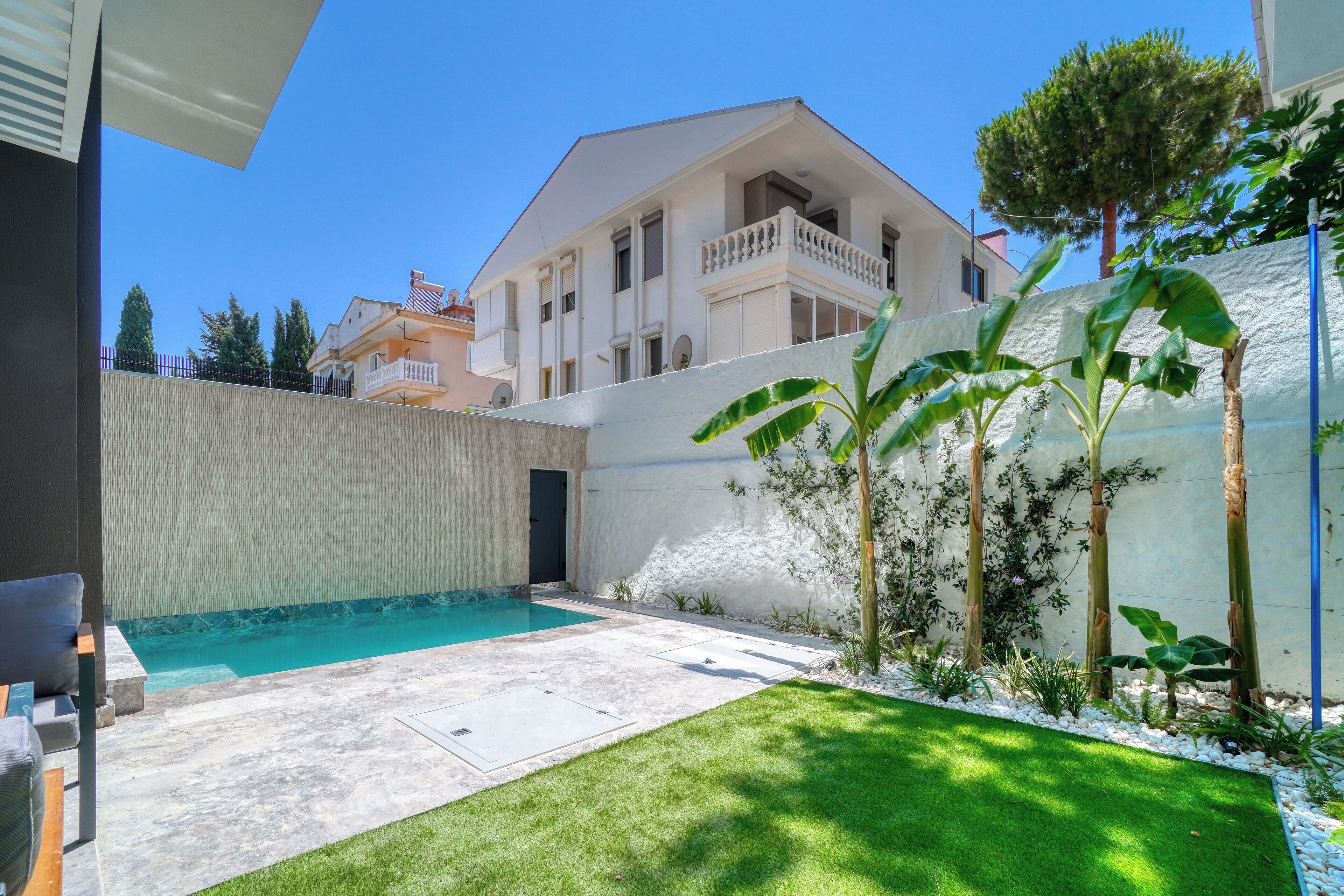 A residential property with a swimming pool, a well-maintained lawn, and a white exterior wall.