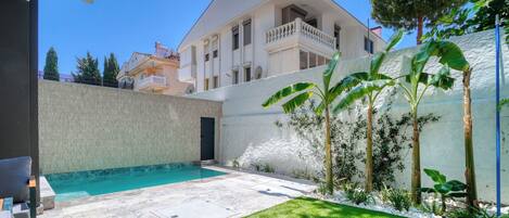 A residential property with a swimming pool, a well-maintained lawn, and a white exterior wall.